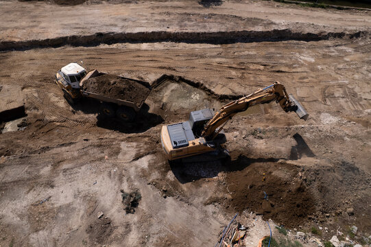 Excavator and dump truck performing earthmoving work at construction site aerial view