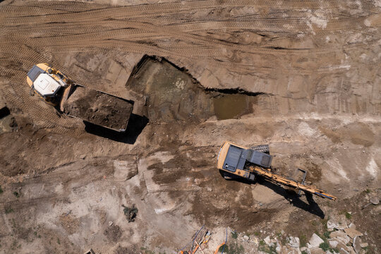 Excavator and dump truck performing earthmoving work at construction site aerial view