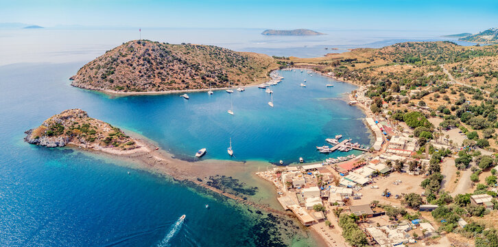 Gumusluk bay aerial view showing boats in the clear turquoise Aegean sea with the small fishing village and surrounding islands in Turkiye