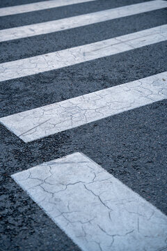 Worn pedestrian crosswalk markings with cracked white paint on asphalt road