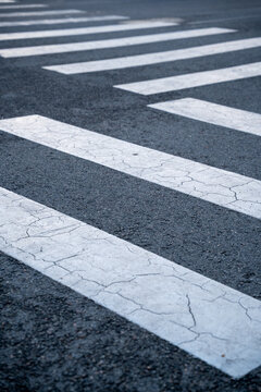 Worn pedestrian crosswalk markings with cracked white paint on asphalt road