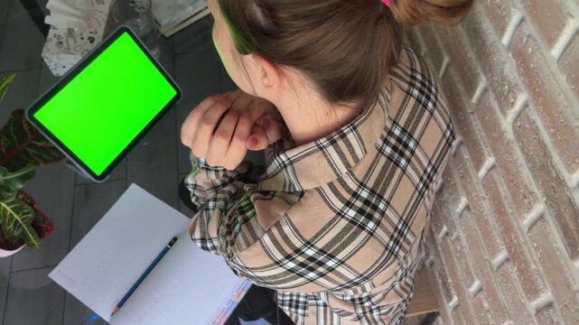Stressed young student attending an online class using a green screen tablet, feeling tired and rubbing her face during a boring lecture in a home schooling environment