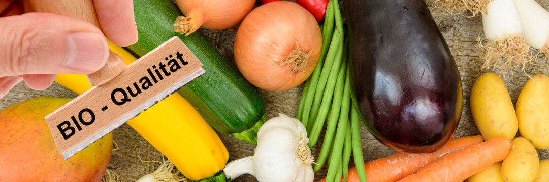 Ein Holzstempel ist beschriftet mit dem Aufdruck: Bio-Qualit&auml;t &uuml;ber frischem Obst und Gem&uuml;se - FOTOMONTAGE