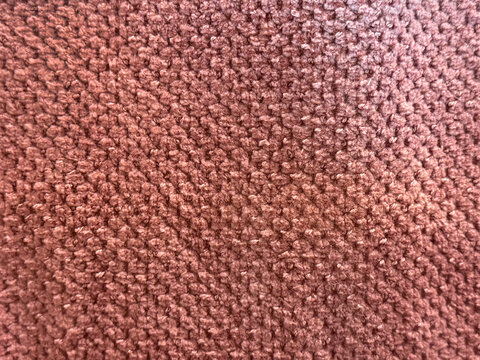 Close up of a soft, textured boucle fabric in a warm terracotta red tone with a dense, bumpy woven surface.