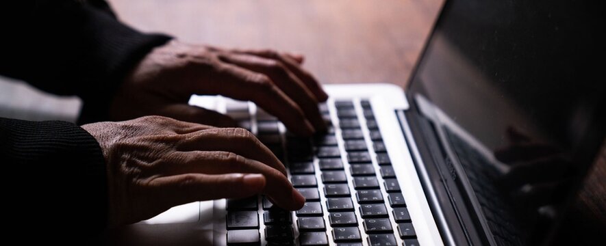 Hands type on laptop keyboard with focused attention. Soft lighting highlights fingers and keys. Dark background draws eye to typing motion. Implies productivity, work, or digital engagement