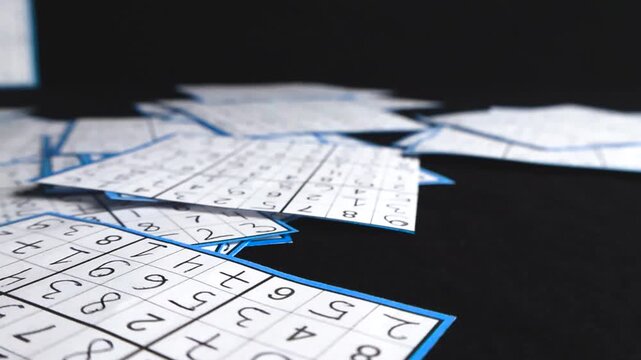 Many paper cut outs of solved sudoku puzzles with handwritten numbers covering a black surface. The camera glides over the intricate numerical grids showing a variety of solutions