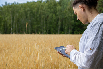 Middle aged farmer looking down at tablet screen while standing among wheat field crops. Digital agriculture concept showing data-driven crop management in the field. © Ina