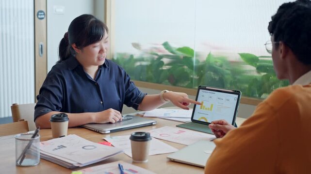 Diverse business colleagues discussing financial data and roadmap strategy on tablet computer in modern office