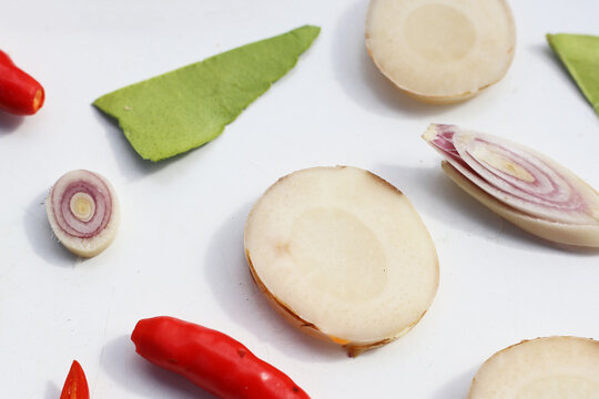 A colorful, close-up pattern of Thai herbs: lime slices, galangal, lemongrass, chilies, and kaffir lime leaves.