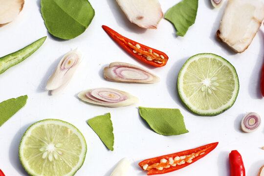 A colorful, close-up pattern of Thai herbs: lime slices, galangal, lemongrass, chilies, and kaffir lime leaves.