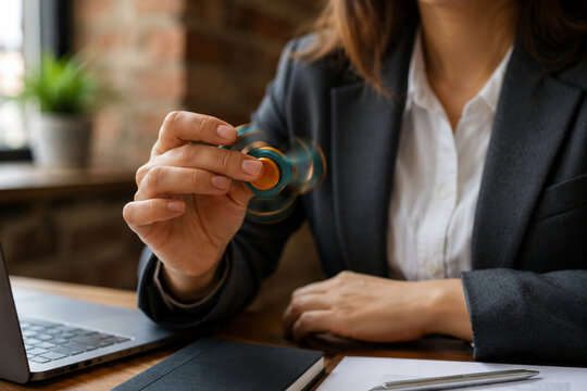 Close-up of hands using a fidget spinner at office desk while working, calm everyday focus habit