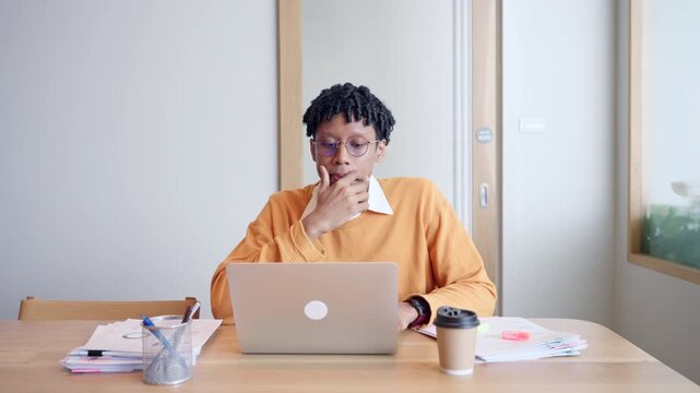 Stressed African American male freelancer feeling tired and rubbing forehead while working on laptop in office