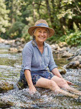 Cheerful Senior Woman Sitting Inside Shallow Running Mountain River Stream