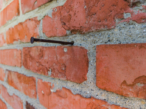 Weathered red brick wall background with an iron nail