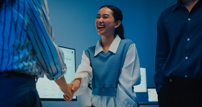 Close up multiracial group young Asia businesspeople in smart casual wear discussing business shaking hand together while stand in modern night office. Partner cooperation, coworker teamwork concept.