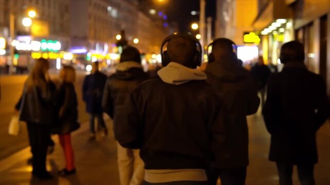 Back view of people walking along a busy city street while wearing headphones, capturing an everyday urban lifestyle moment that reflects commuting, movement, anonymity, modern technology, and daily r