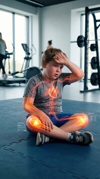 Tired child sitting in gym with holographic digital visualization of heart and joint stress. Medical analysis of physical activity and health. Fitness monitoring and body scan technology.
