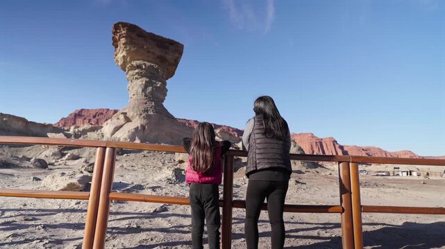 Mother and daughter admire El Hongo in Ischigualasto Provincial Park, San Juan Province, Argentina, sharing a family travel experience beside the iconic desert rock formation, camera slide.