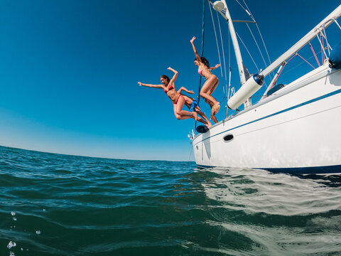 Happy friends diving from sailing boat into the sea - Travel and summer vacation concept - Soft focus on blond girl face - UGC wide lens content