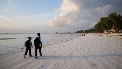 Chłopcy idący plażą do szkoły  o wschodzie słońca Zanzibar Tanzania © kubikactive