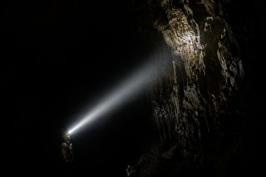 A single beam of light from a helmet lamp illuminates a dark cave.