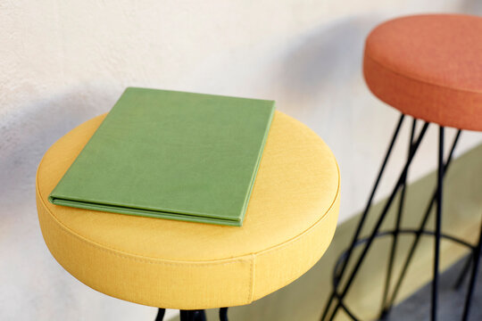 Closed green menu folder on yellow fabric bar stool in modern restaurant caf&eacute; interior