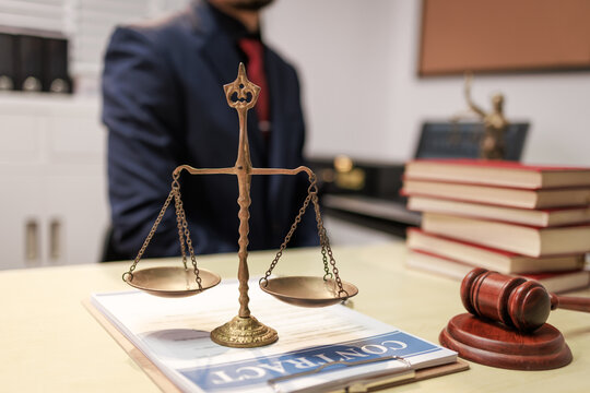 Scales of justice on a lawyer&rsquo;s desk with gavel, books, and a blurred attorney in the background, law, fairness, and legal advice.