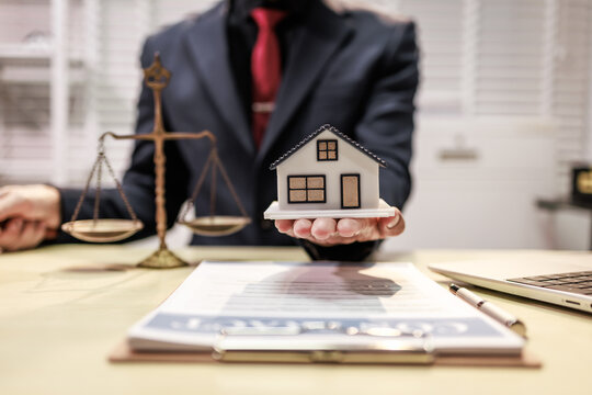 Lawyer holding a small house model beside scales of justice, suggesting real estate law, property disputes, and legal advice.