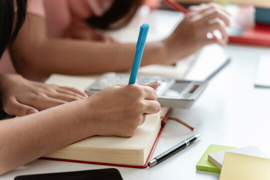 Asian female students writing in notebook while preparing for upcoming education assignment