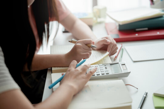 Asian female students writing in notebook while preparing for upcoming education assignment