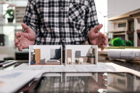 Person presenting two small room design models on a table with floor plans, an interior design project in a workshop or office