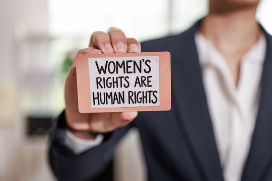 A person in a business suit holds a card reading women's rights are human rights, activism, equality, and social justice