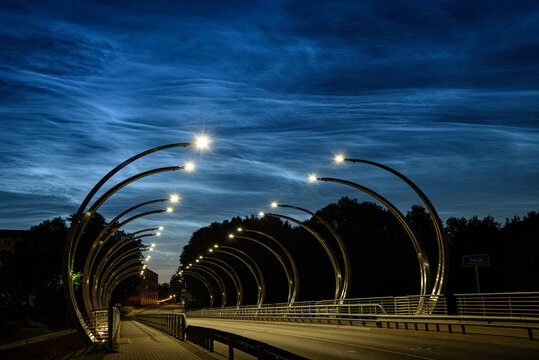 Valmiera Latvia-July 16,2026-Modern illuminated bridge at blue hour with glowing street lights, dramatic clouds, and an empty road creating a striking urban perspective.