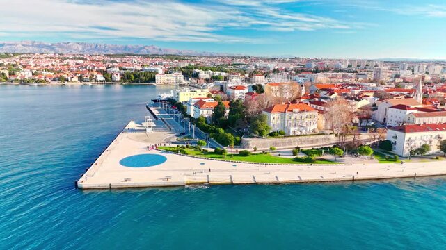 Smooth drone flyby along Zadar's waterfront showcasing the Sea Organ, Greeting to the Sun, historic old town, calm Adriatic Sea and visitors enjoying a sunny day.