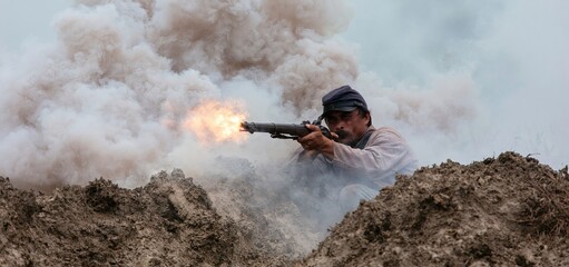 Fototapeta premium Amidst thick smoke and mud, a Civil War soldier fires his rifle in a vivid battle reenactment.