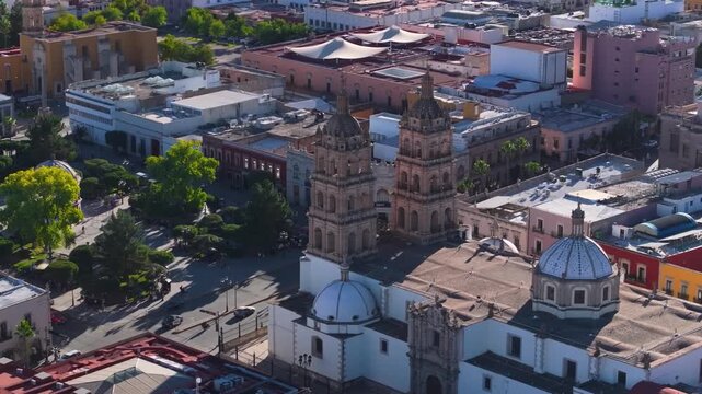 A refined, aerial close-up showcasing the ornate facade of the Cathedral Basilica of Durango adjacent to the bustling Plaza de Armas.