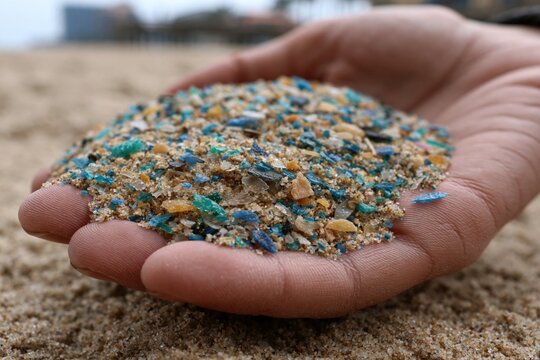 Hand holding microplastic and sand polluting beach environment