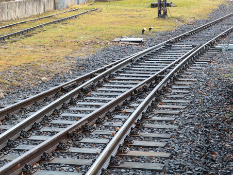 A pair of parallel metal railway tracks curves across a gravel bed, illustrating infrastructure and connectivity in a rural setting where steel rails guide public transportation travel