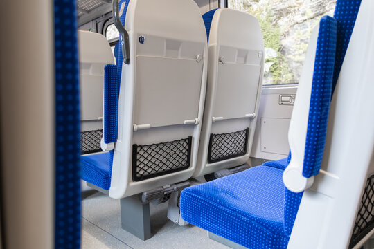 Empty blue passenger seats inside a modern commuter train carriage, depicting comfortable public transportation travel with a clean interior design and natural light for urban commuting