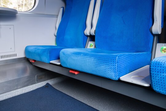 Empty blue upholstered train seats with white pull-out tables in a modern carriage, representing clean public transportation infrastructure for travel, tourism and daily commuter transit