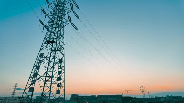 High voltage electricity transmission tower silhouette against sunset sky over Japanese suburban residential area, slow pan