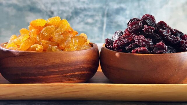 Golden and dark jumbo raisins in wooden bowls shown during a slow leftward camera movement on a rustic tabletop