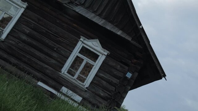 Old wooden rural house with weathered log walls and decorative white window frame