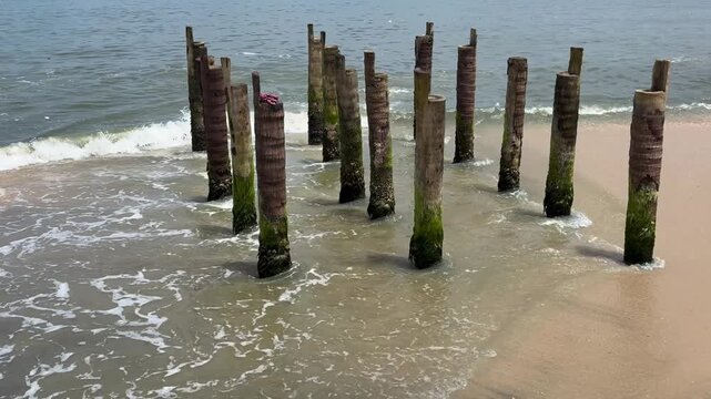 Ocean waves crashing against the wooden piers on a sandy beach