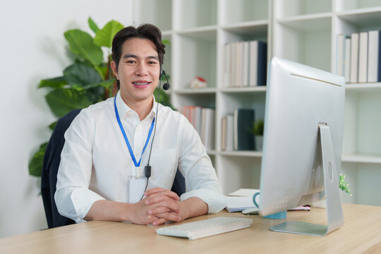 Asian male customer service representative with headset sitting at office desk