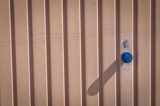 A beige corrugated metal garage door with a blue knob and lock cylinder in sunlight