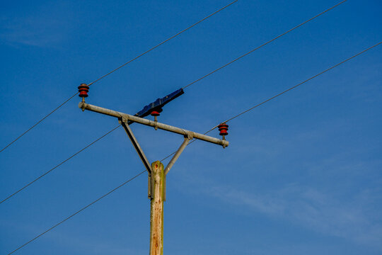An old wooden utility pole with red insulators and overhead power lines against blue sky