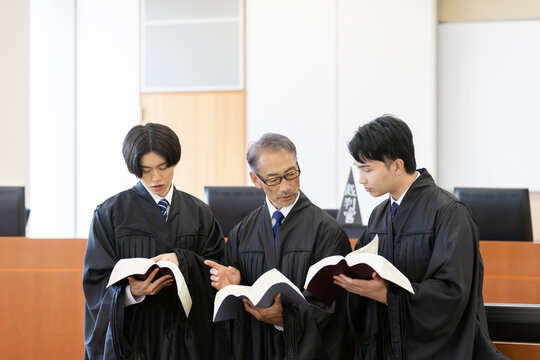 法廷で六法全書を確認しながら打ち合わせをする日本人裁判官3人