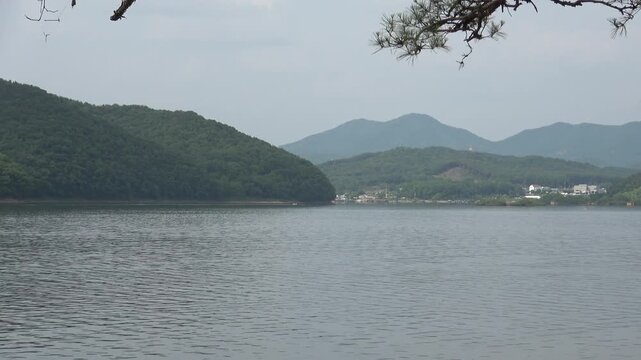 4K Scenic lakeside village under green hills with tree branches in the upper frame