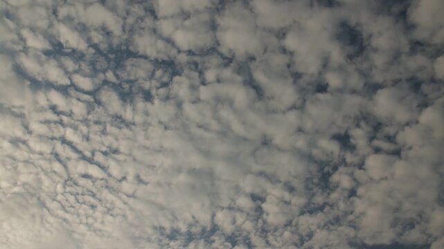Time-lapse of small white clouds moving across blue sky and gradually covering the sky